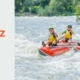 Vier Personen steuern gemeinsam ein Rafting-Boot durch schäumende Flusswellen und beweisen Team-Resilienz, um gemeinsam stark zu bleiben.