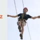 Zwei Personen balancieren gesichert auf einem Hochseil-Parcours und reichen sich die Hände, um gegenseitiges Vertrauen und psychologische Sicherheit im Team zu stärken.